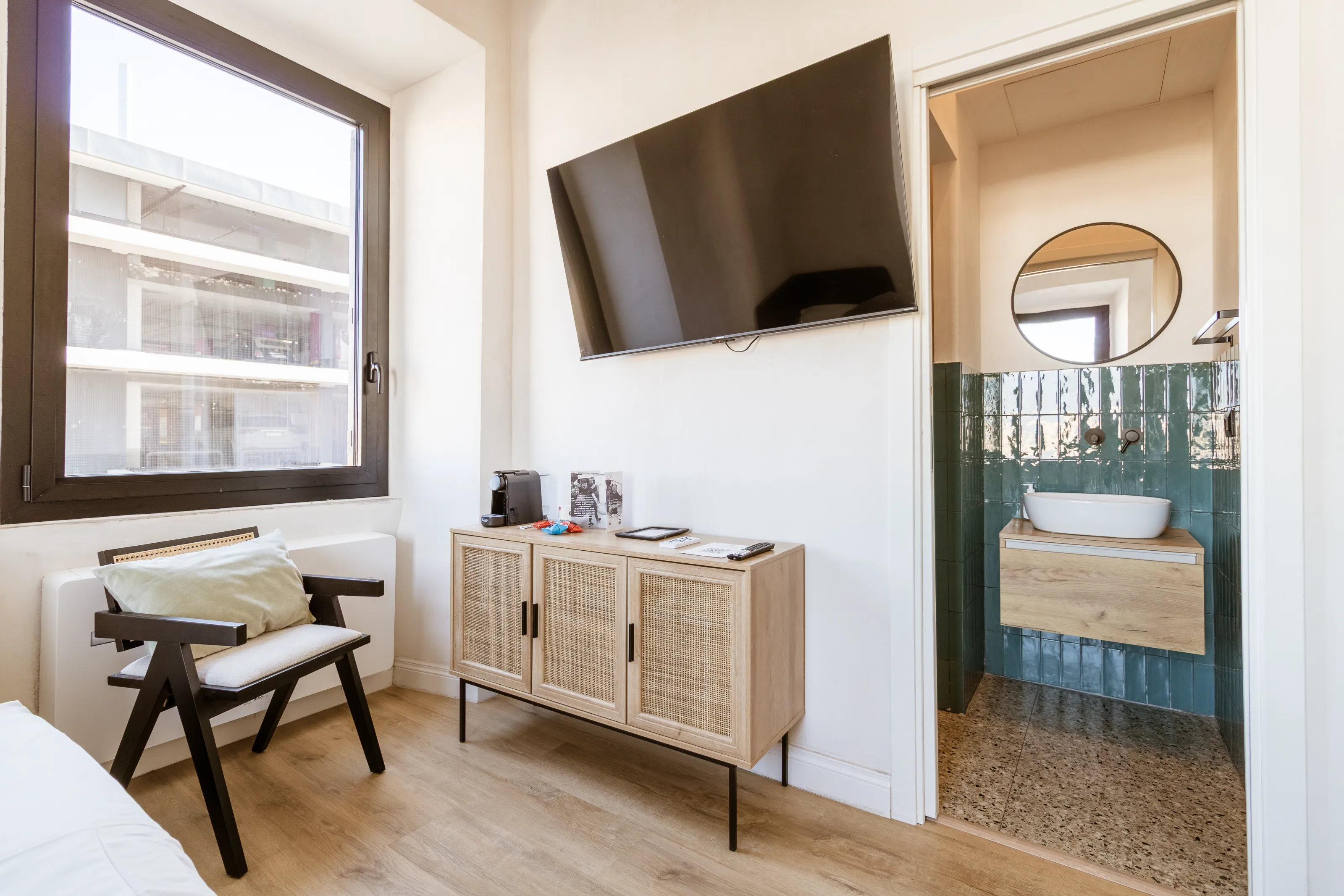 Cozy corner with a design chair, wooden cabinet, and flat-screen TV, featuring a stylish bathroom in view