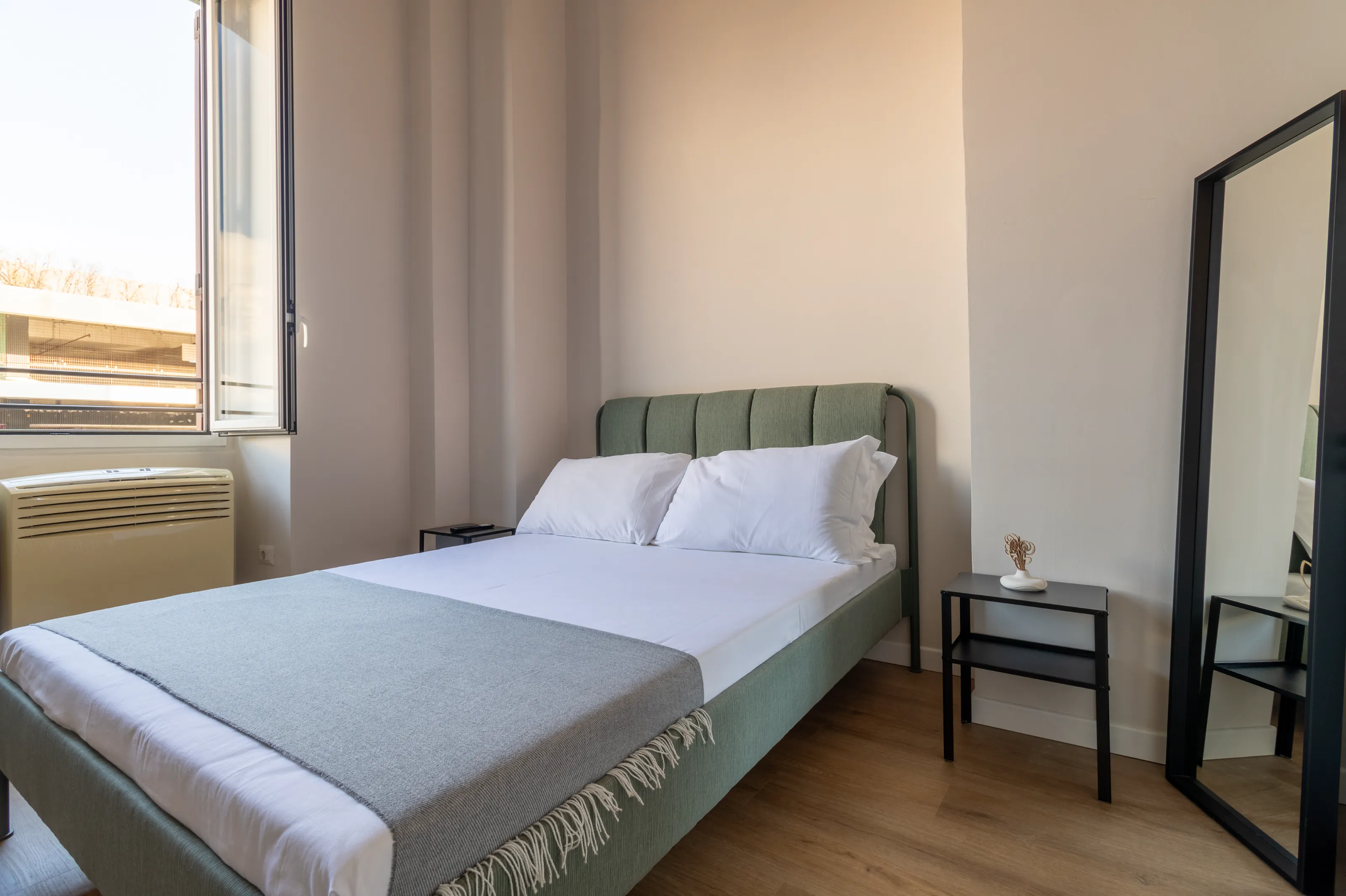 Bright bedroom with a double bed and large windows, furnished in a modern and minimal style