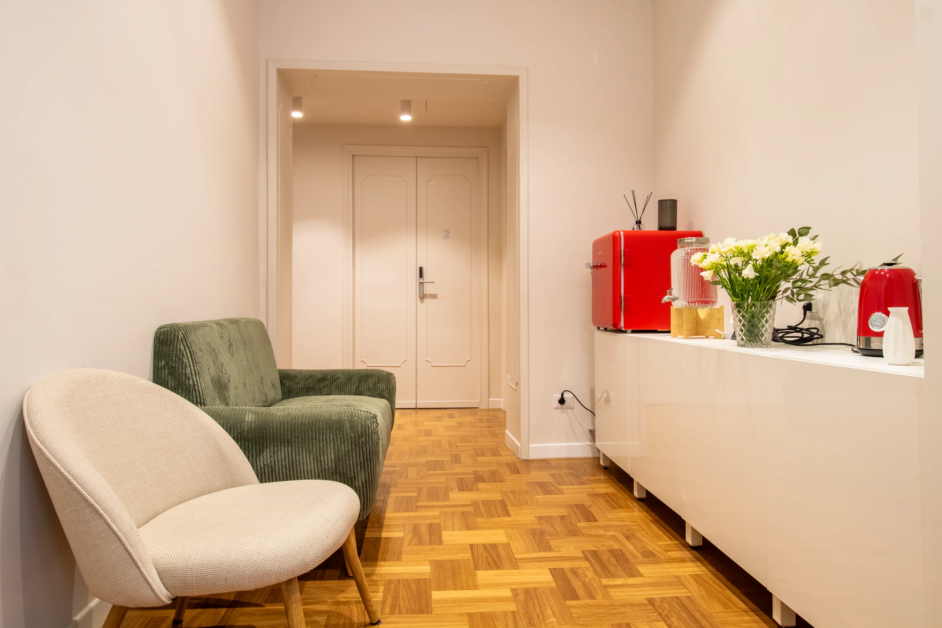 A cozy corner of the common lounge with a green sofa, armchair, coffee station, and fresh flowers.