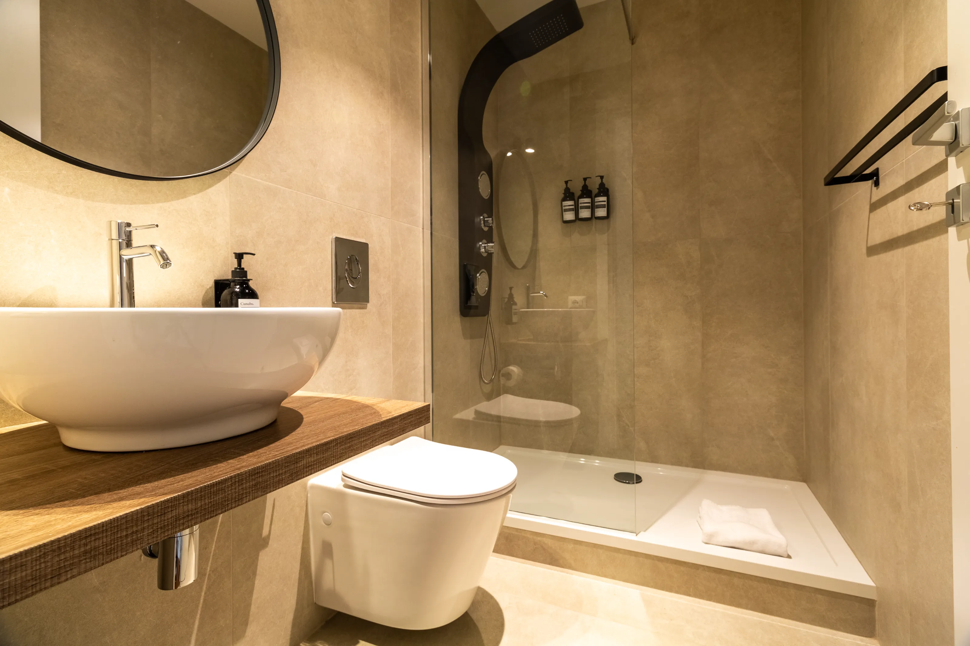 Modern bathroom with a walk-in shower, beige finishes, and wall-mounted dispensers.